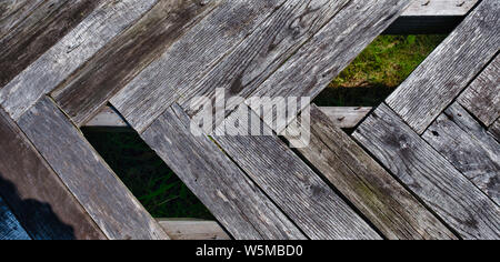 Weathered, graying wooden planks arranged in a herringbone pattern, with some planks missing Stock Photo