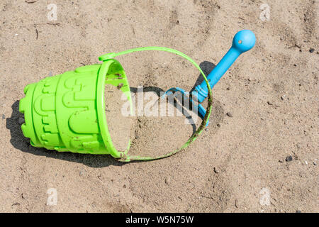 Sand toys, a blue shovel and a bright green pail, are out in the sand on a sunny beach in the summer. Stock Photo