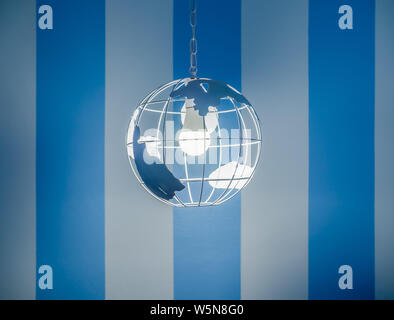 Modern global earth world shape ceiling lamp on white and blue striped wall background. Stock Photo