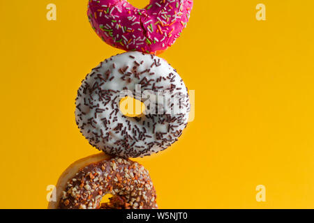 multicolored sweet donuts with sprinkles on vibrant yellow background copy space Stock Photo
