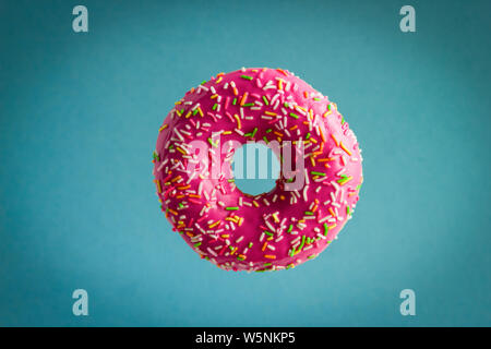 sweet donut with pink berry chocolate icing and sprinkles flying on blue background Stock Photo