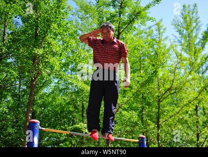 70-year-old Chinese man Nie Yinmin binds and fixes his feet on a horizontal bar to have 360-degree rotations at a park in Shenyang city, northeast Chi Stock Photo