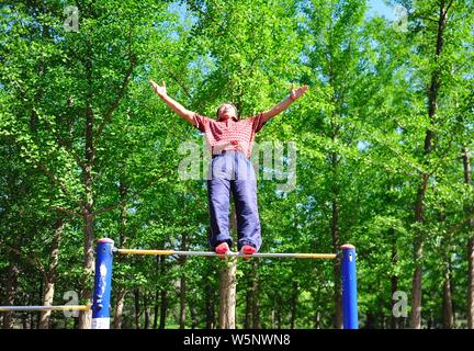 70-year-old Chinese man Nie Yinmin binds and fixes his feet on a horizontal bar to have 360-degree rotations at a park in Shenyang city, northeast Chi Stock Photo