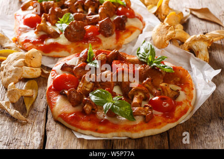 Portioned italian pizza with chanterelle mushrooms, mozzarella cheese, tomatoes and basil close-up on parchment on the table. horizontal Stock Photo