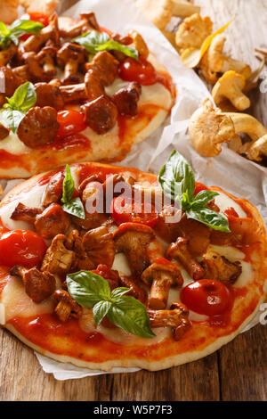 Mini pizza with chanterelle mushrooms, mozzarella cheese, tomatoes and basil close-up on the table. vertical Stock Photo