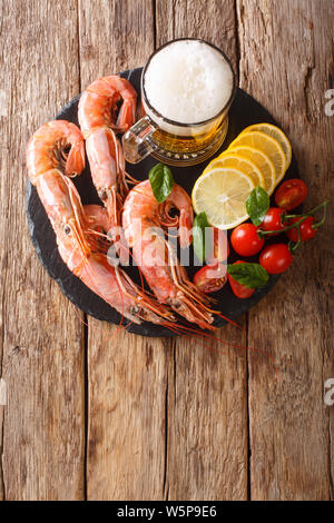 Delicious king prawns with light beer, lemon and tomatoes close-up on a slate board on the table. Vertical top view from above Stock Photo