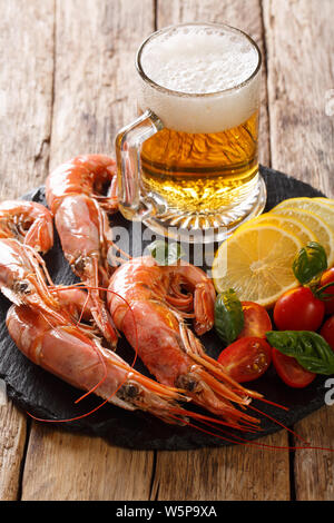 glass of beer and delicious shrimps, lemon and tomatoes close-up on a slate board on the table. Vertical Stock Photo