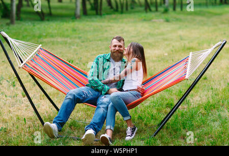 Young couple with mobile phone sitting on hammock. Stock Photo