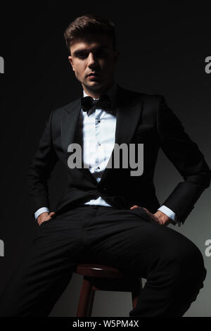 relaxed elegant man sits on wooden chair with hands in pockets, portrait picture Stock Photo