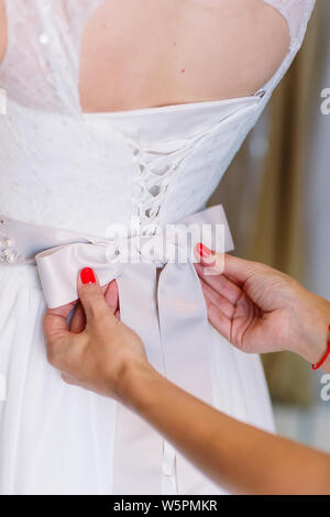 Female trying on wedding dress in a shop with women assistant. Stock Photo