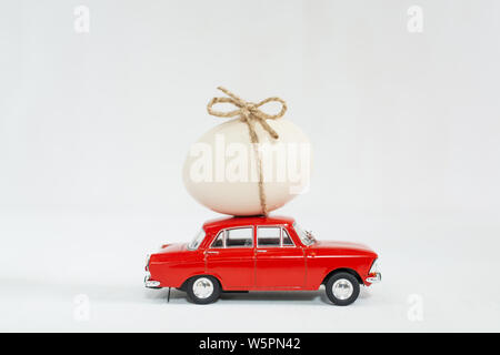 Red vintage toy car with chicken egg on the roof. Isolated image on white background. Stock Photo
