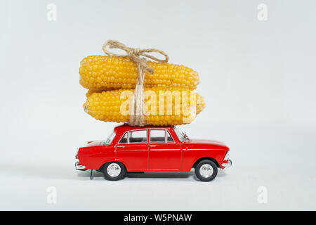Red vintage toy car with small yellow corn cobs on the roof. Isolated image on white background. Stock Photo