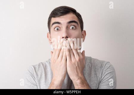 close-up portrait of a white man with a surprised, shocked face covers his mouth with his hands Stock Photo
