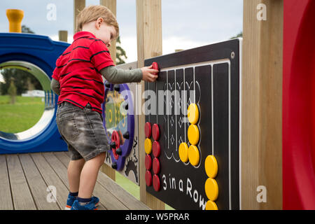 A young preschool child plays with the activities attached to the climbing frame at the new Foster Park Playground in Rolleston, New Zealand Stock Photo