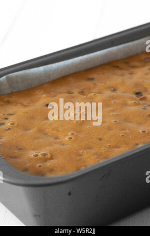 Fruit cake loaf mixture in a metal baking tin.  On a white wood background Stock Photo