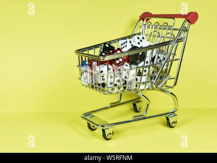 Bunch of different size and color dice placed inside a miniature metallic shopping cart , isolated on yellow background, conceptual image Stock Photo