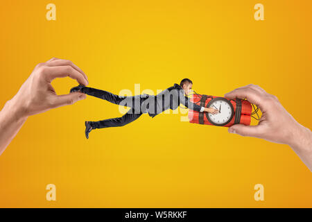 Two hands, holding small businessman who is clutching with his both hands at dynamite time bomb, which is also in one of the hands. Stock Photo