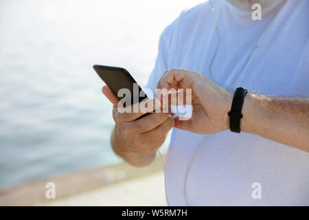 Senior man as runner with fitness tracker at the riverside. Caucasian male model using gadgets while jogging and cardio training in summer's morning. Healthy lifestyle, sport, activity concept. Stock Photo