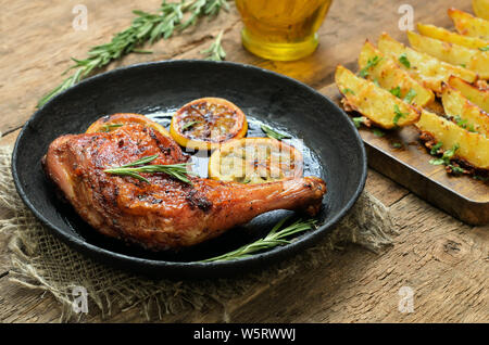 Chicken leg with vegetables and herbs, potato wedges on wooden table Stock Photo