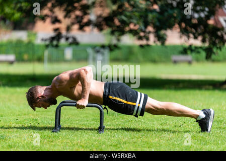 Fit athlete man doing push up with push-up bars on the floor, outdoor  sport and training in grass concepts Stock Photo