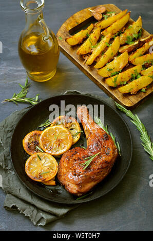 Roasted chicken leg with vegetables and herbs, potato wedges on wooden table Stock Photo