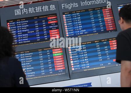 --FILE--Chinese passengers look at an electronic display showing information of flights which have been delayed or cancelled due to a heavy rainstorm Stock Photo
