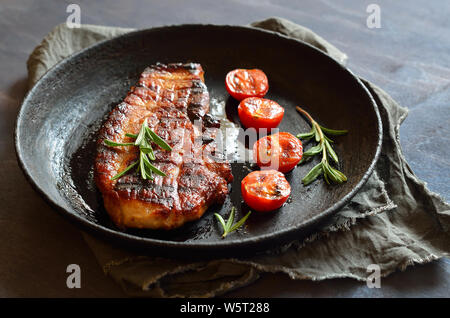 Fried pork steak and tomatoes in frying pan Stock Photo