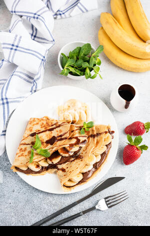 French crepe with chocolate and banana filling on white plate decorated with chocolate sauce and fresh mint leaf, table top view Stock Photo