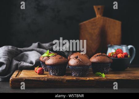 Group of chocolate muffins or cupcakes on wooden board, black background. Food still life Stock Photo