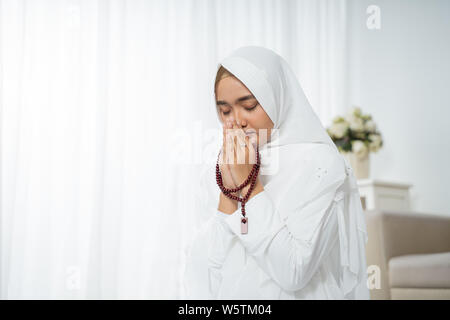 asian young woman praying with Al-Qur'an and prayer beads Stock Photo