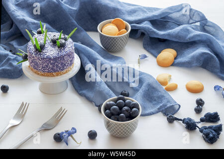 Two round no bake strawberry mini cheesecakes with salt caramel and halfs of strawberries, embellished with real blue blossoms. Blue wooden table. Stock Photo