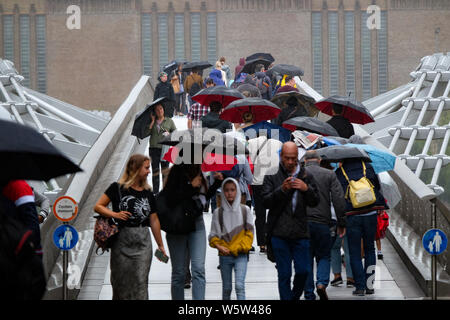 Millennium Bridge, London, UK. 30th July 2019. Umbrellas up and heavy showers as people cross the Millennium Bridge. Credit: Matthew Chattle/Alamy Live News Stock Photo