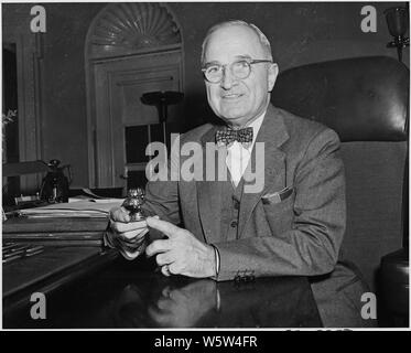 Photograph of President Truman at his desk in the Oval Office, holding a four-leaf-clover paperweight. Stock Photo