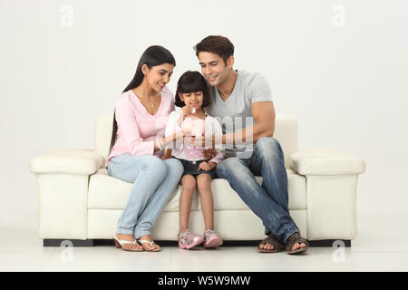 Girl putting coin into a piggy bank with her parents Stock Photo