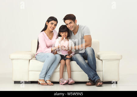 Girl putting coin into a piggy bank with her parents Stock Photo