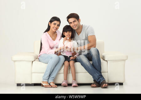 Girl putting coin into a piggy bank with her parents Stock Photo