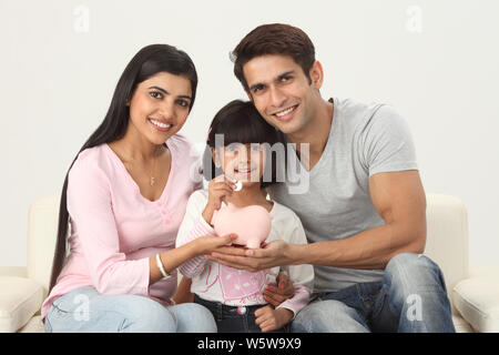 Girl putting coin into a piggy bank with her parents Stock Photo