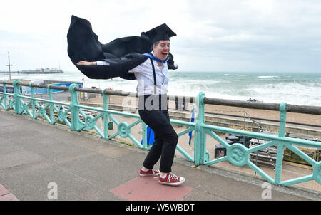 Brighton, UK. 30th July, 2019. Emily Green hangs on to her gown after graduating from the University of Brighton as she celebrates on a very windy seafront afterwards . Credit: Simon Dack/Alamy Live News Stock Photo