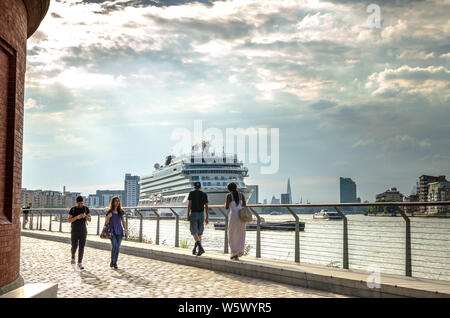 Tourists by the River Thames with MV Viking Sky cruise ship in the background at Greenwich, London Stock Photo