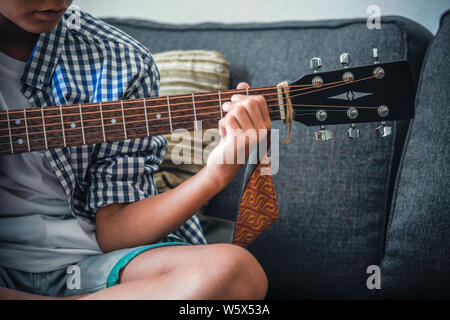 Close up image of a young hand plays acoustic guitar. Close-up view of a trendy child playing a beautiful melody with his musical instrument. Hands pl Stock Photo