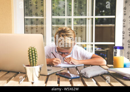 Beautiful young boy doing homework outdoor. Child working with pencil and laptop at home after school. Kid studying on the terrace during holiday drin Stock Photo
