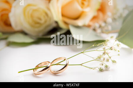 Pair of wedding gold rings with dry flowers and roses on white Stock Photo