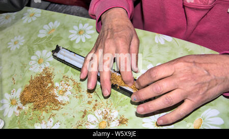 Making cigarettes handmade using rollers and tobacco on a table at home. Stock Photo