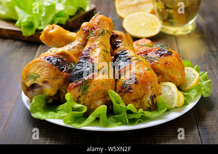Roasted chicken drumsticks on lettuce leaves on wooden table Stock Photo