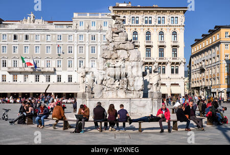 People sitting at fountain of four continents on Plaza Unita on sunny spring day in Trieste, Italy, April 2019 Stock Photo