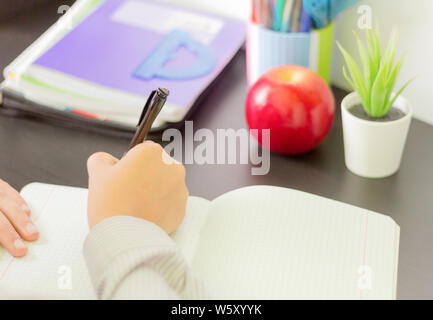 the student writes in a workbook, doing homework at the table Stock Photo
