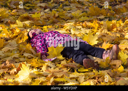 Little girl laying on ground in autumn park Stock Photo