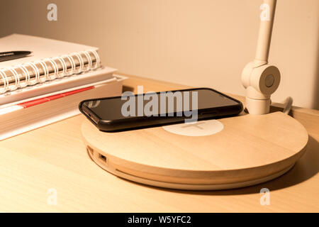 Smartphone in black case charging wireless on bed table Stock Photo