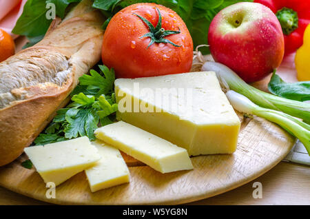 A horizontal shot of a delicious quick snack of a ploughman’s lunch with French bread mature cheese a fresh tomato and an apple. Stock Photo