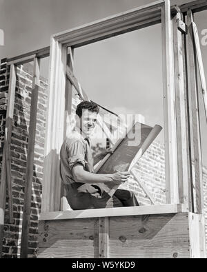 1940s SMILING YOUNG MAN CARPENTER CONSTRUCTION WORKER SITTING IN FRAMED HOUSE WINDOW READING BLUEPRINT PLANS LOOKING AT CAMERA - b11688 HAR001 HARS JOY LIFESTYLE JOBS CARPENTER PLANS COPY SPACE HALF-LENGTH PHYSICAL FITNESS PERSONS INSPIRATION MALES RISK PROFESSION CONFIDENCE B&W EYE CONTACT FREEDOM GOALS SUCCESS SKILL OCCUPATION HAPPINESS SKILLS CHEERFUL STRENGTH CUSTOMER SERVICE CAREERS CHOICE EXCITEMENT EXTERIOR PROGRESS PRIDE IN OPPORTUNITY AUTHORITY OCCUPATIONS SMILES CONNECTION CONCEPTUAL FRAMED JOYFUL STYLISH PRECISION YOUNG ADULT MAN BLACK AND WHITE CAUCASIAN ETHNICITY HAR001 Stock Photo